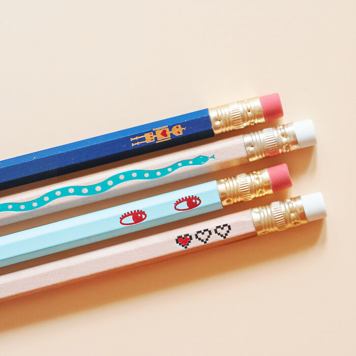 Four handmade projects pencils with unique designs: a blue pencil with geometric shapes, a beige one with a snake, a light blue one with eyes, and another beige one with hearts.