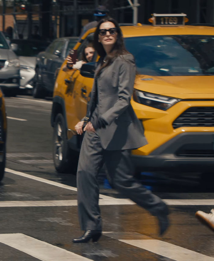 Woman in a gray suit and sunglasses crossing street with yellow taxi in the background, illustrating working for the Vogue icon.