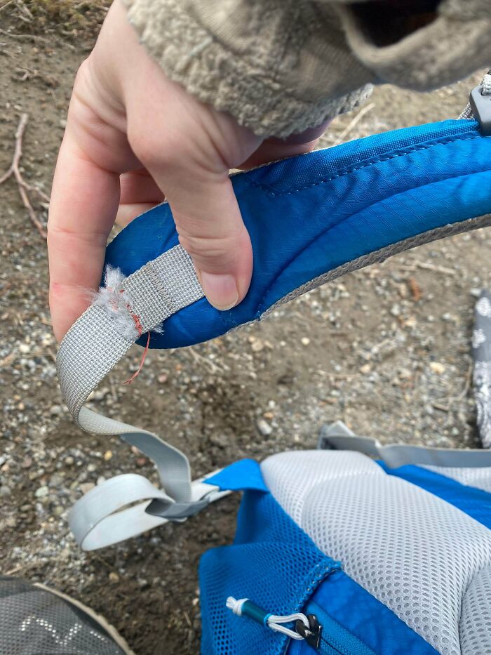 A hand holding a torn blue backpack strap, showing a clever solution to fix it with random junk.