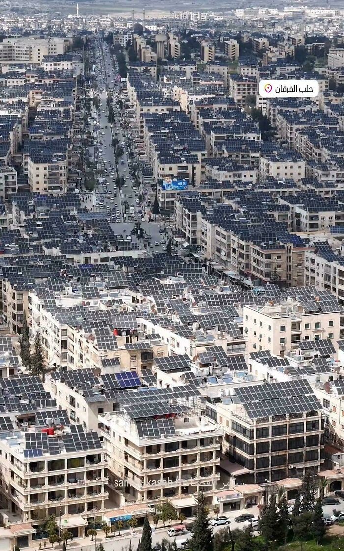 A cityscape covered densely with solar panels on rooftops under cloudy sky