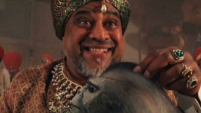 A man with a turban and jewels smiling, holding a monkey, showcasing hilarious nonsensical movie details.