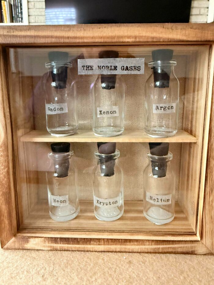 A handmade wooden display case holds six small bottles labeled with Noble Gases, a project showing patience and talent.
