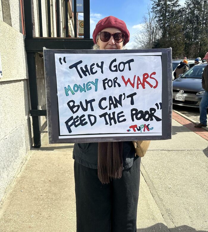 Woman holding protest sign about money for wars versus feeding the poor, highlighting dystopian issues in the United States.