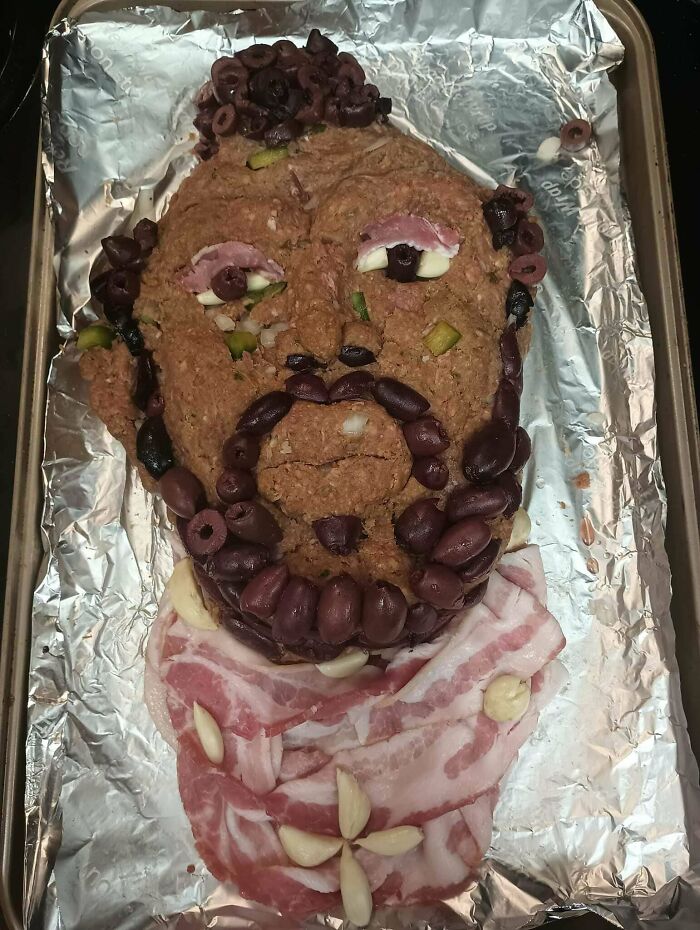 A bizarre meatloaf head on foil, with olives for hair/beard and bacon for a scarf. A true Bananasausage food crime.