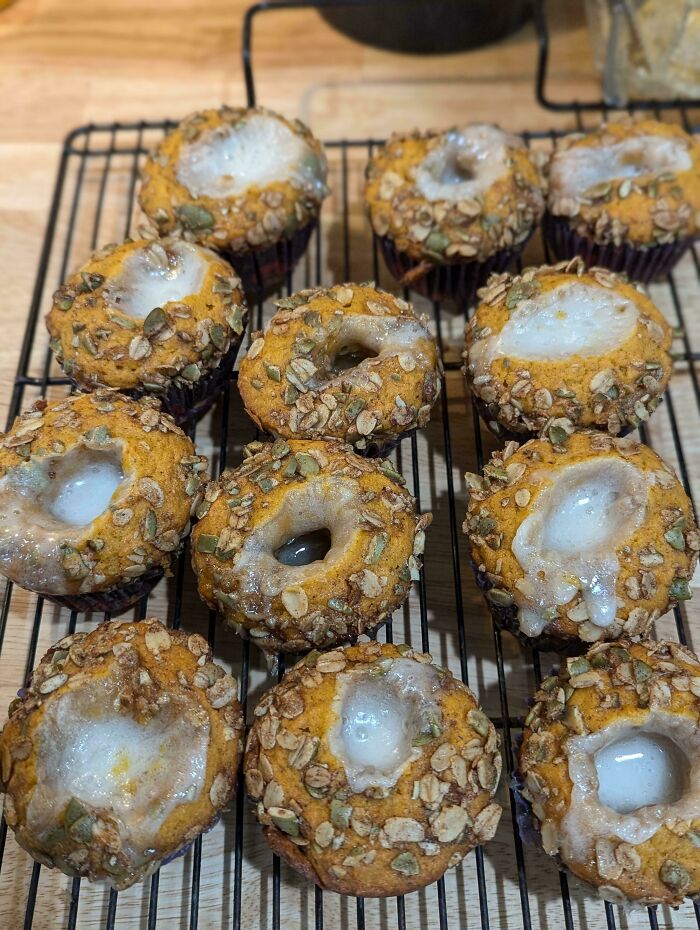 A dozen pumpkin muffins on a rack, some with holes, glazed and topped with oats and seeds. A Bananasausage food crime.