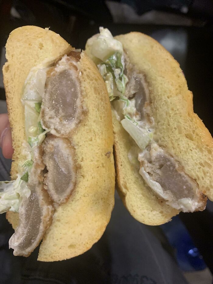 A sliced bananasausage sandwich with pale meat, white sauce, and lettuce on a yellow bun, hinting at food crimes.