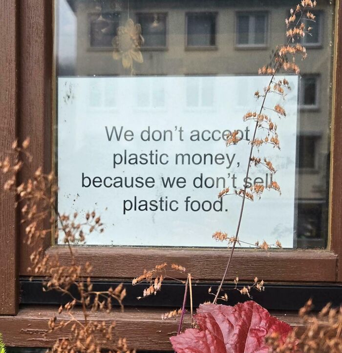 Sign on a window stating they don’t accept plastic money because they don’t sell plastic food, funny confusing sign.