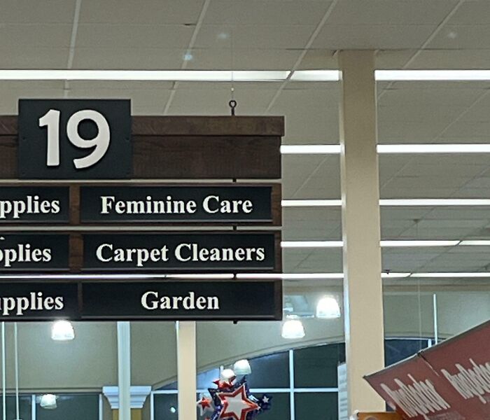 A confusing funny store aisle sign showing feminine care, carpet cleaners, and garden supplies together.