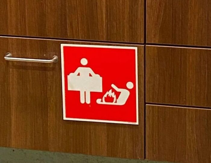 Confusing and funny sign showing a person holding a large object next to someone on fire on a wooden wall panel.