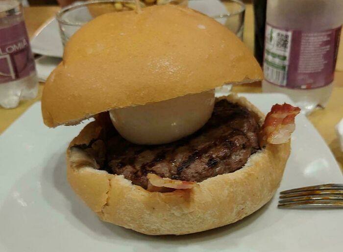 A hamburger in a round bun with a poached egg and bacon, a Bananasausage food crime.