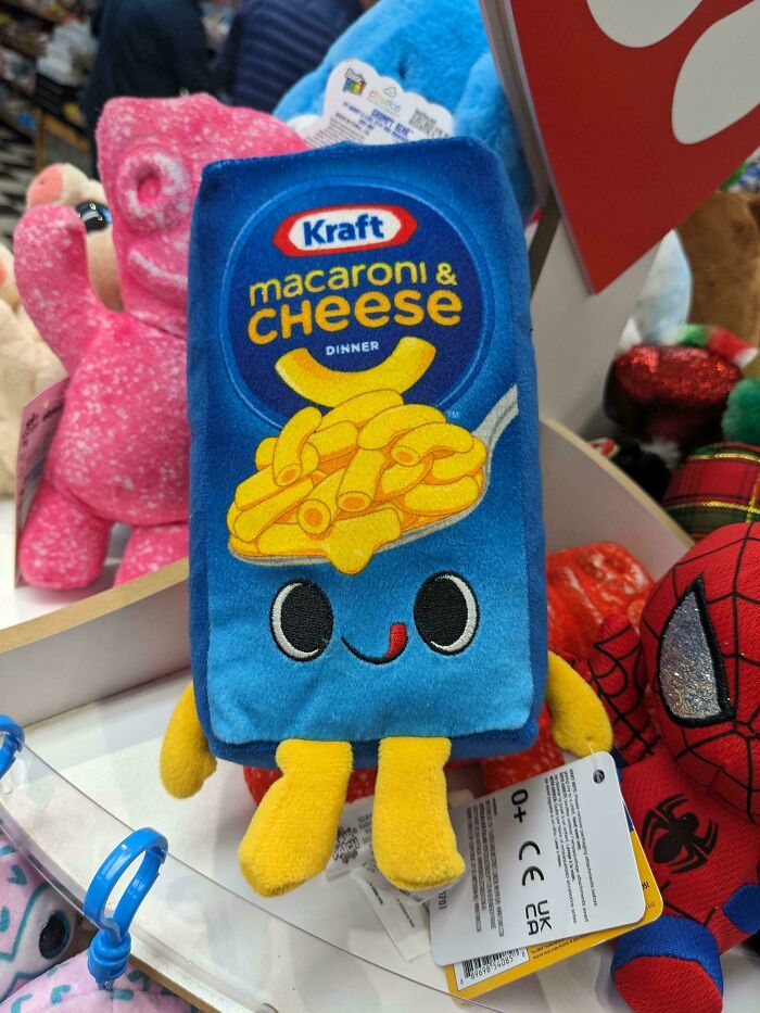 Plush Kraft macaroni and cheese toy with smiling face among colorful stuffed animals in a store display.