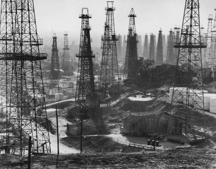 Black and white photo of an eerie urban oil field with numerous tall drilling towers