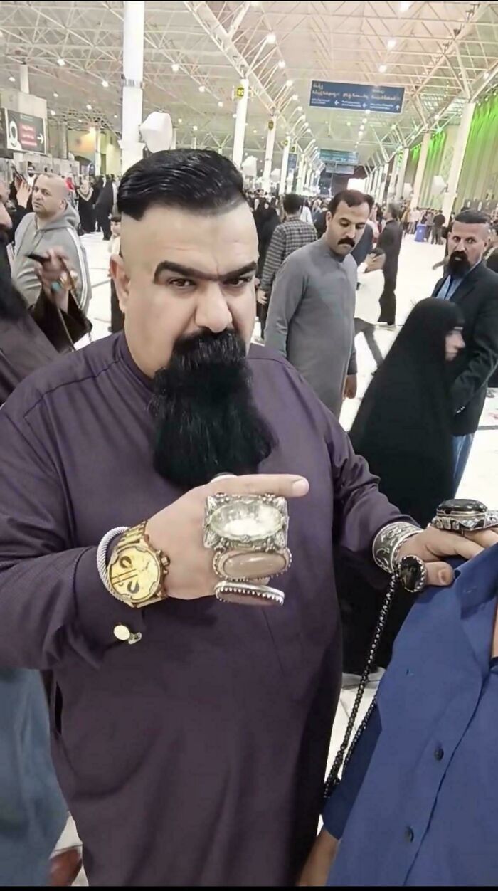 A man with a large beard, a unique shaved haircut, and many rings and bracelets on his hands.