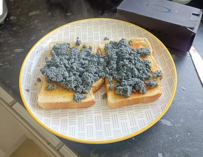 Two slices of toast on a plate topped with a grey, crumbly substance, resembling a bananasausage food crime.