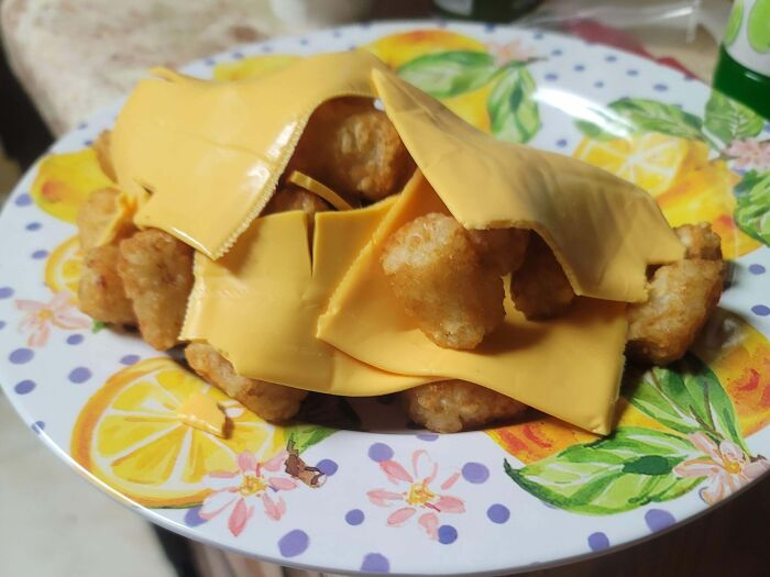 A plate of golden tater tots covered with slices of American cheese, a true food crime of bananasausage proportions.
