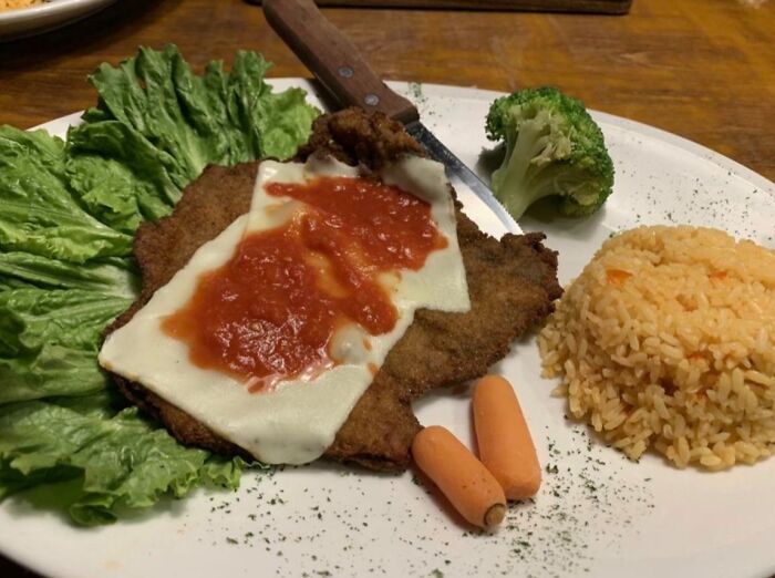 A breaded cutlet topped with cheese and marinara, served with rice, broccoli, carrots, and lettuce, a possible food crime.