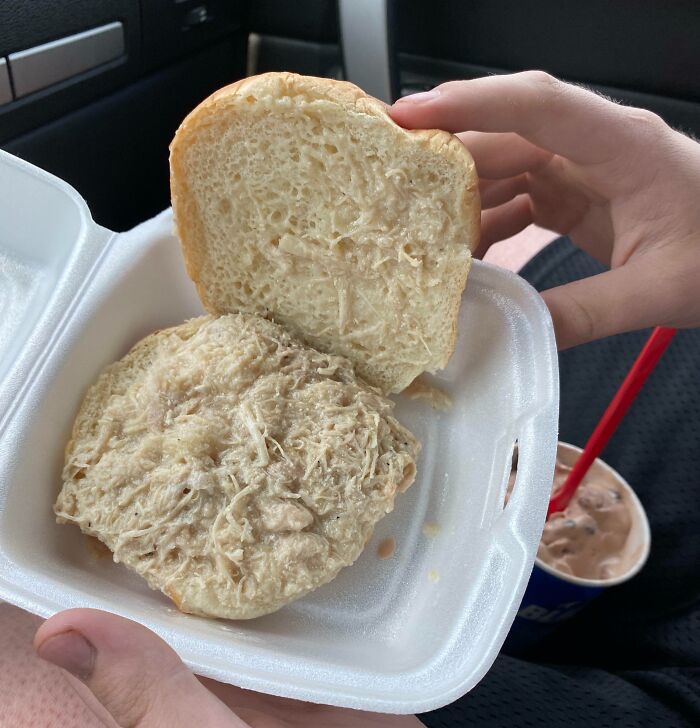 A Bananasausage sandwich in a styrofoam container, with a person holding it and a milkshake nearby. A true food crime!