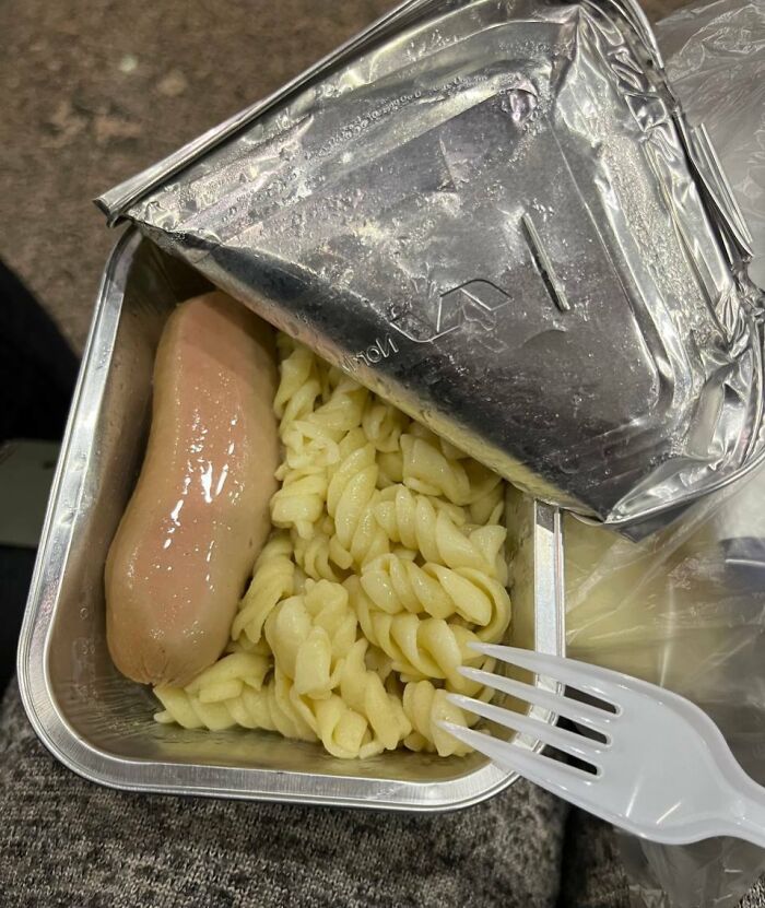 A sad-looking Bananasausage and pasta meal in an opened foil tray with a plastic fork, a true food crime.