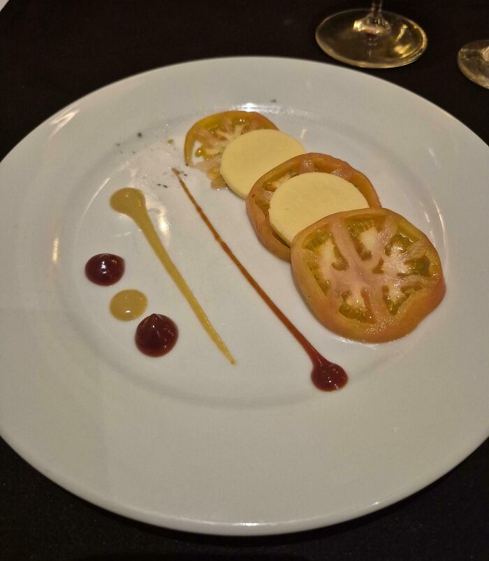 A white plate with sliced tomatoes and what appears to be rounds of bananasausage, drizzled with sauces.