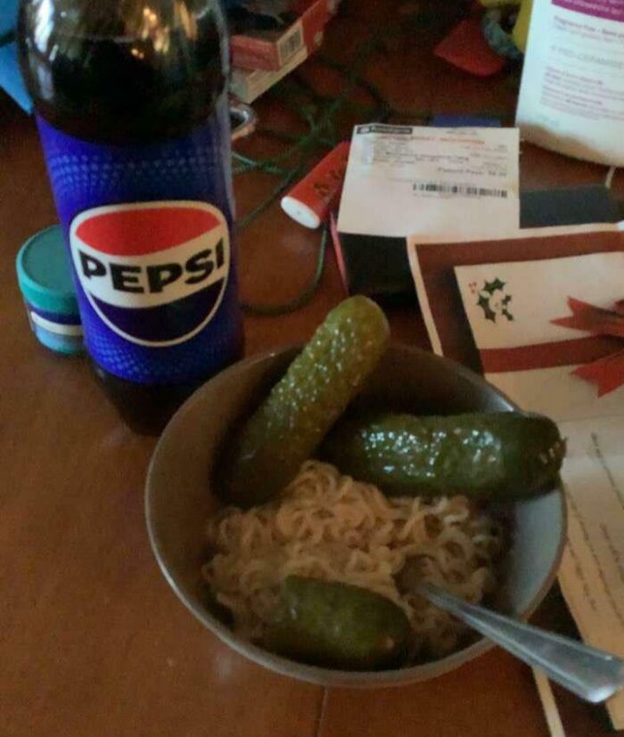 A bowl of ramen with three whole pickles, a Pepsi, a true food crime.