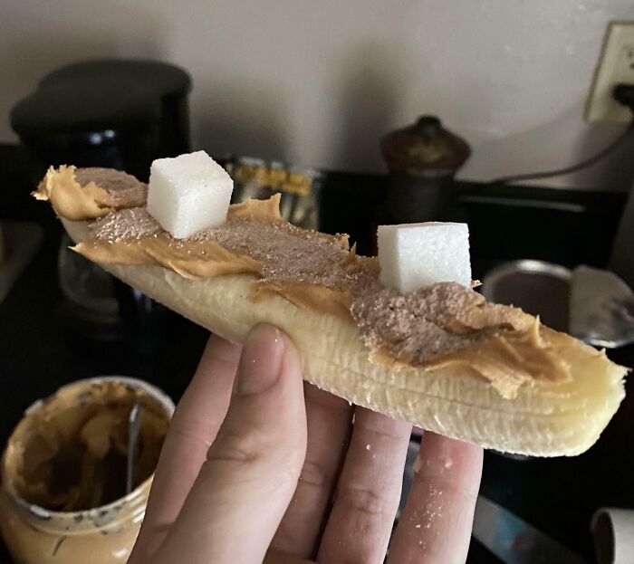 A hand holds a "bananasausage" of banana, peanut butter, cocoa powder, and sugar cubes. A true food crime.