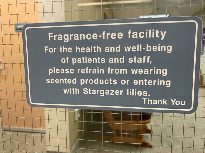A blue sign on a wire fence: "Fragrance-free facility. Please refrain from wearing scented products or entering with Stargazer lilies. Thank You." This sign reminds of oddly specific rules.