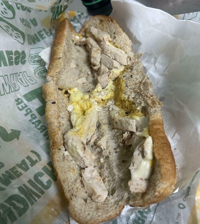 A Bananasausage-like "food crime" sandwich with chicken and yellowish sauce on whole wheat bread, wrapped in paper.