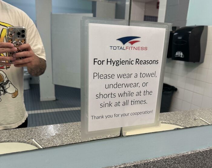 A TotalFitness sign reflects in a mirror: "Please wear a towel, underwear, or shorts at the sink for hygienic reasons."