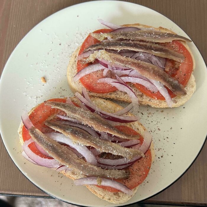 Two slices of bread topped with tomatoes, red onions, and anchovies, a food crime for some.