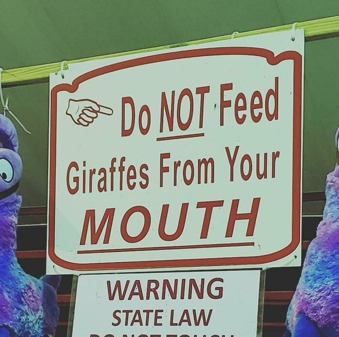 A sign with red text: Do NOT Feed Giraffes From Your MOUTH, a strangely specific rule that makes you wonder about its origin.