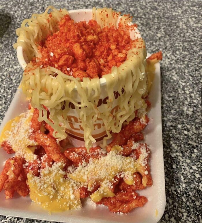 A Bananasausage-level food crime: a cup of instant ramen overflowing with crushed Cheetos and cheese sauce, on a foam tray.