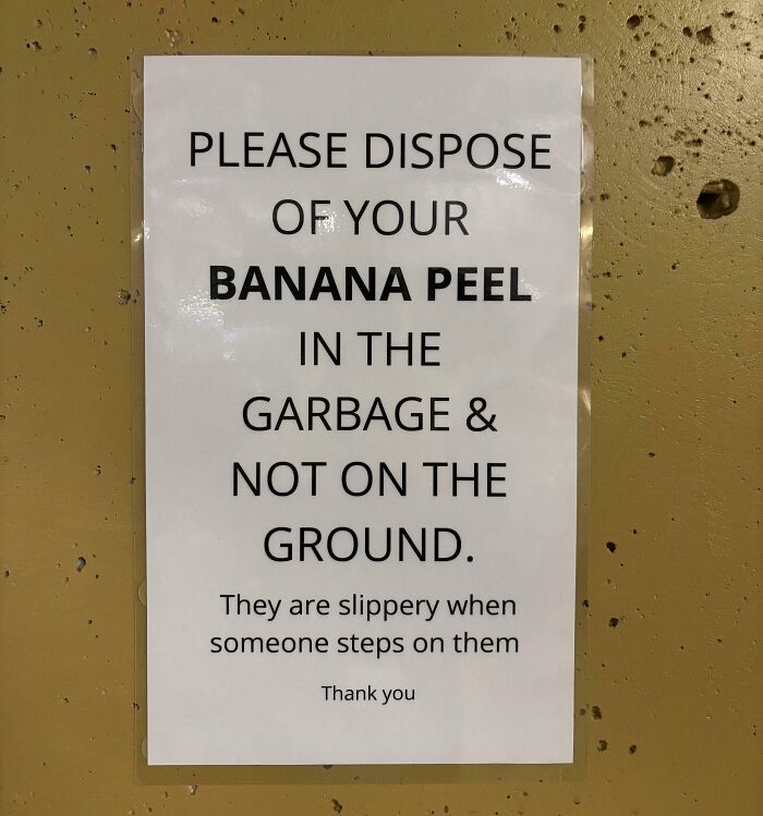 A white sign on a golden-brown wall, stating to dispose of banana peels in the garbage, not on the ground due to slipping. An example of oddly specific rules.