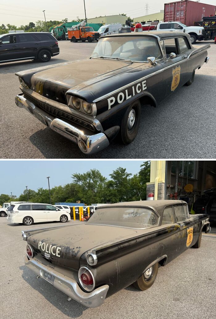 Old dusty black police car parked outside a mechanic shop, showing wear and vintage design details.
