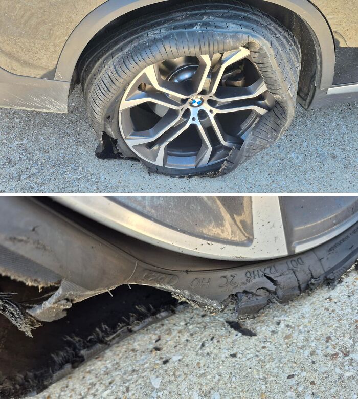 Severely damaged car tire with shredded rubber and exposed wheel rim on a gravel surface during mechanic inspection.