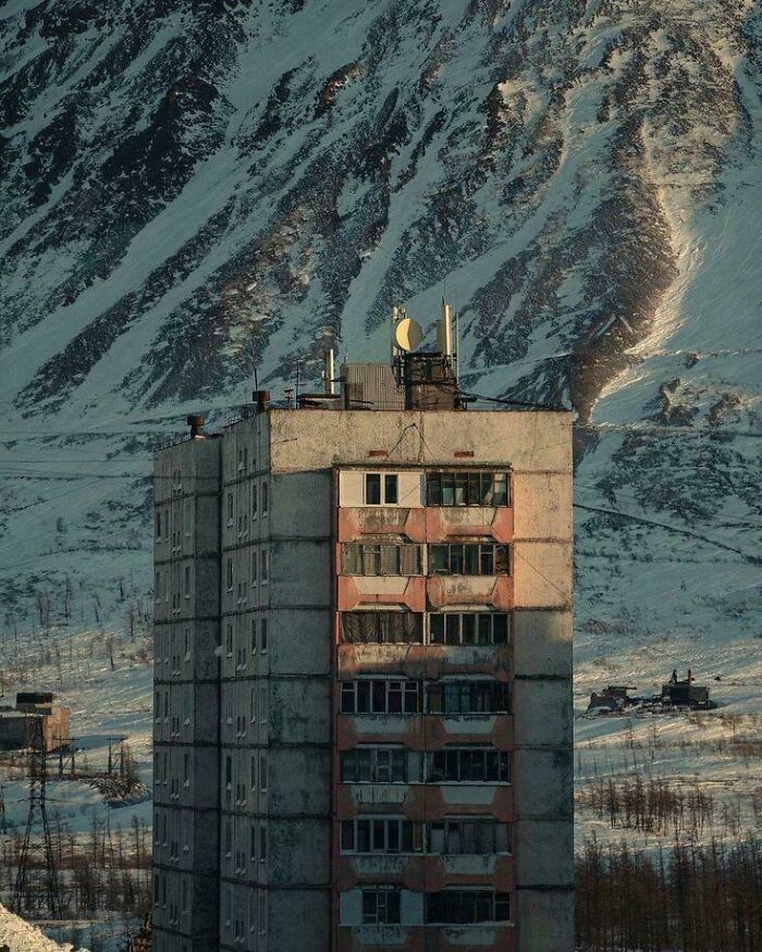 Dilapidated apartment building in urban hell against snow-covered mountain backdrop