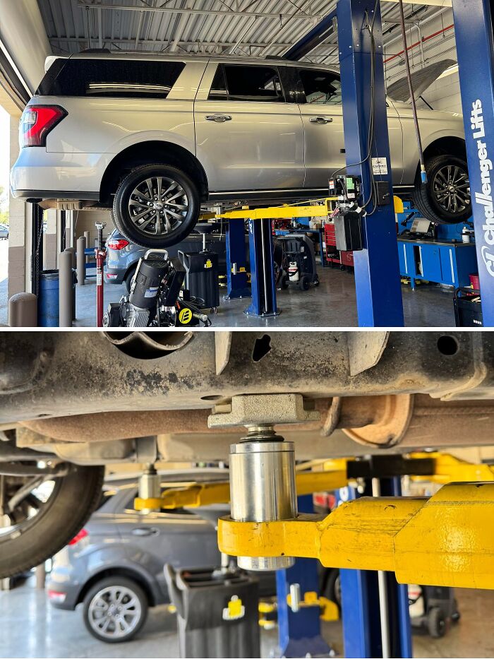 Silver SUV lifted by car mechanics on a hydraulic lift showing underside suspension details in an auto repair shop.