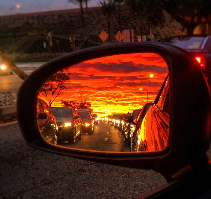 A vibrant, fiery sunset reflected in a car's rearview mirror, showing traffic in a line. A satisfying picture for a gentle reset.