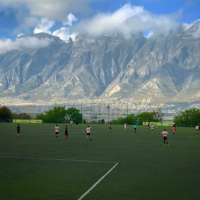 A soccer game on a green field with majestic mountains and clouds in the background, a gentle reset button for your day.