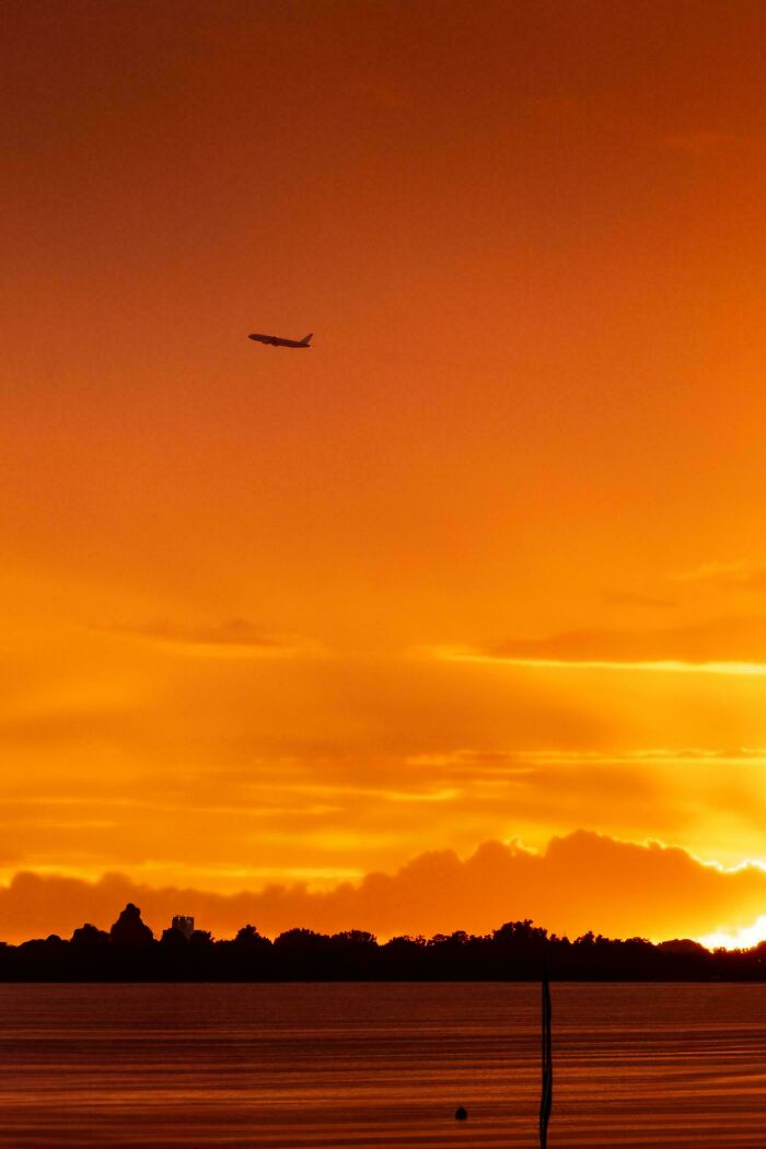 A plane flies across an orange sunset sky over a dark landscape and water, a gentle reset button for your day.
