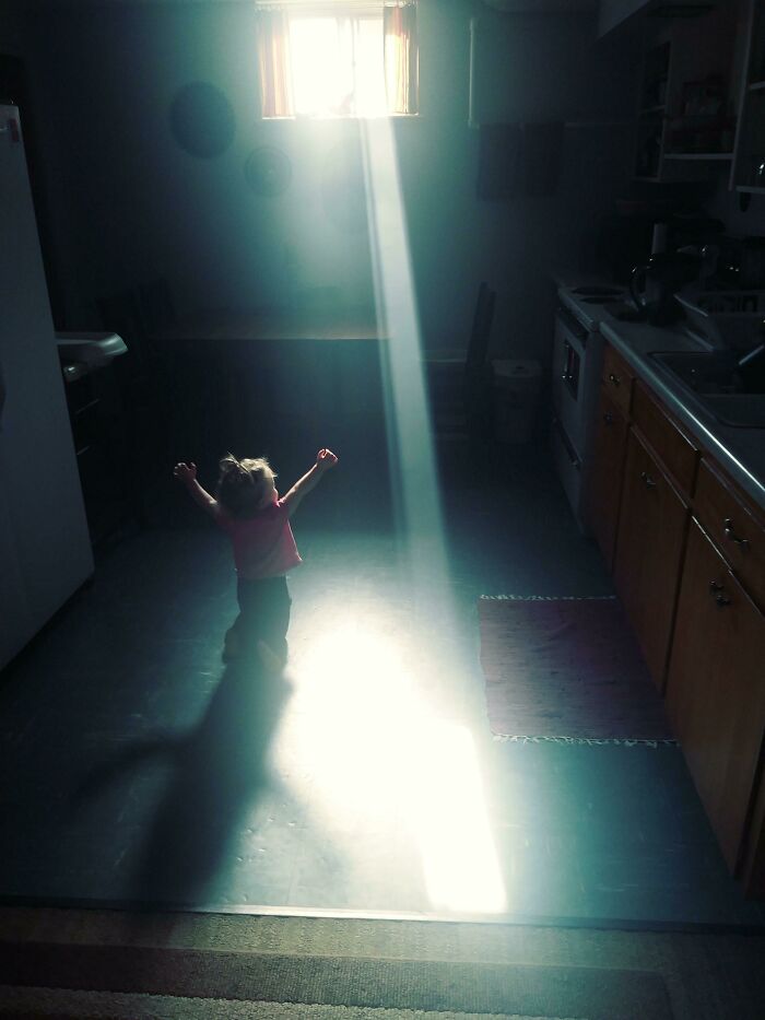 A small child bathed in a sunbeam from a window, arms raised in a moment of gentle reset.
