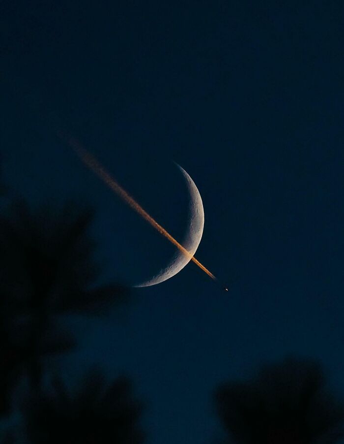 A crescent moon in a dark blue sky, crossed by a luminous orange airplane contrail, offering a gentle reset.