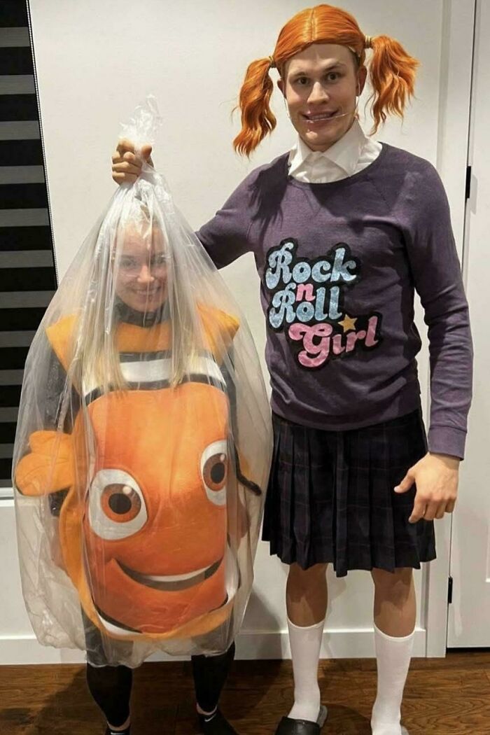 Two people in weird costumes, one inside a plastic bag as a fish, the other in a skirt and wig, creating a confusing cursed image.