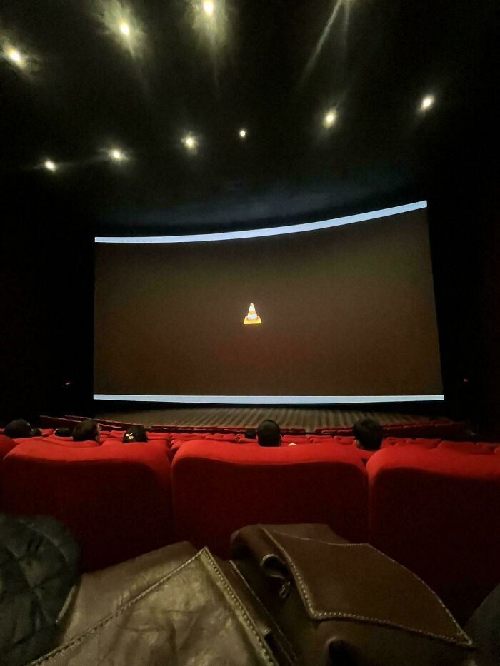 Movie theater screen displaying a confusing VLC cone icon instead of a film, viewed from red seats in a dark room.