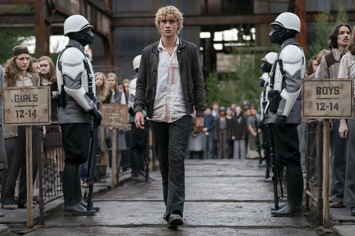 Young male walking between guards in a scene from The Hunger Games, recreating an iconic moment from the new trailer.