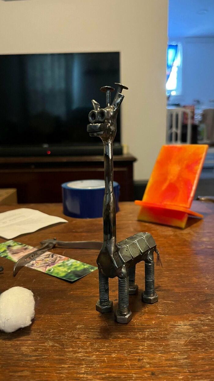 A detailed handmade sculpture of a giraffe made from nuts and bolts stands on a wooden table, showcasing talent.