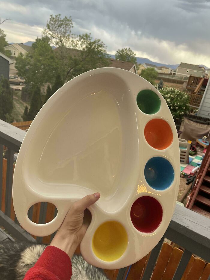A hand holding a white artist's palette shaped plate with colorful dips, a fun thrift store jackpot.