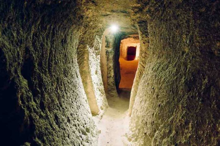 Narrow ancient underground tunnel illuminated by a single light, evoking mysterious events and urban myths atmosphere.