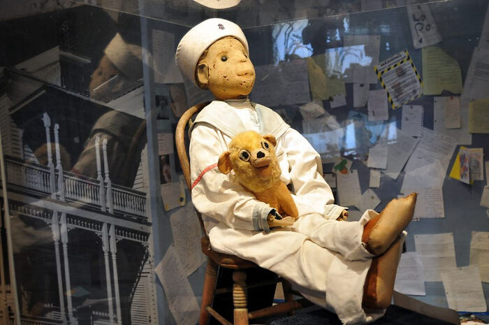 Vintage sailor doll holding a stuffed dog, displayed among mysterious events and urban myths exhibits.