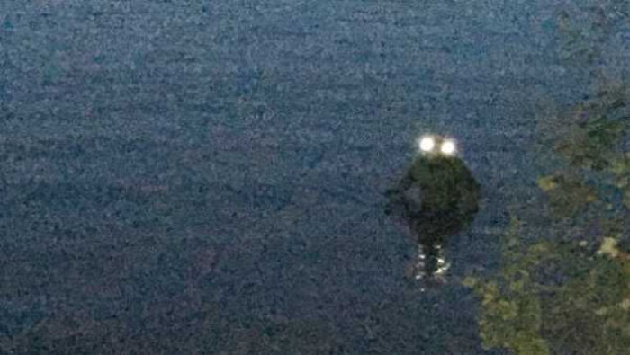 Blurry night image showing mysterious glowing eyes reflecting light over dark water, illustrating mysterious events and urban myths.