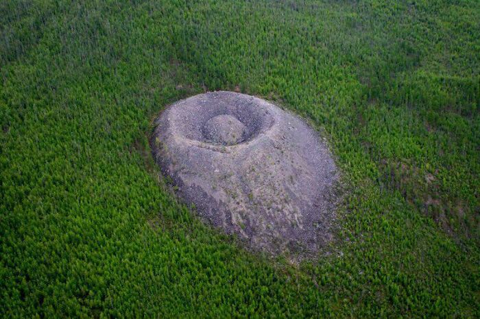 Aerial view of a mysterious geological formation surrounded by dense forest, highlighting unexplained urban myths and events.